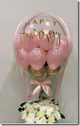 Small pink balloons stuffed in a transparent balloon with 12 white flowers basket