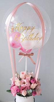 Pink and white balloons stuffed inside a transparent balloon with messahappy birthday tied to a basket with 10 pink flowers
