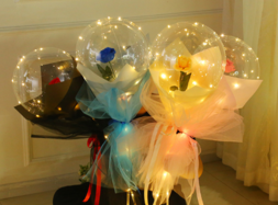 4 roses in four bubble balloons with same coloured wrapping on stick of each balloons wrapped with led lights