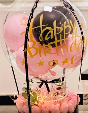 Happy birthday print on the transparent balloon with small pink and black balloons stuffed inside in a box of 20 pink roses beads string and string lights black ribbons