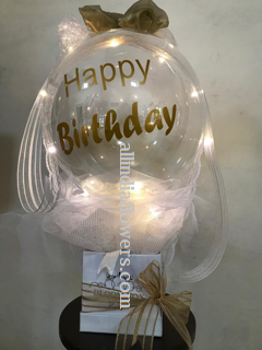 Happy birthday print on the transparent balloon white net wrapping and gold bow in a box and LED lights